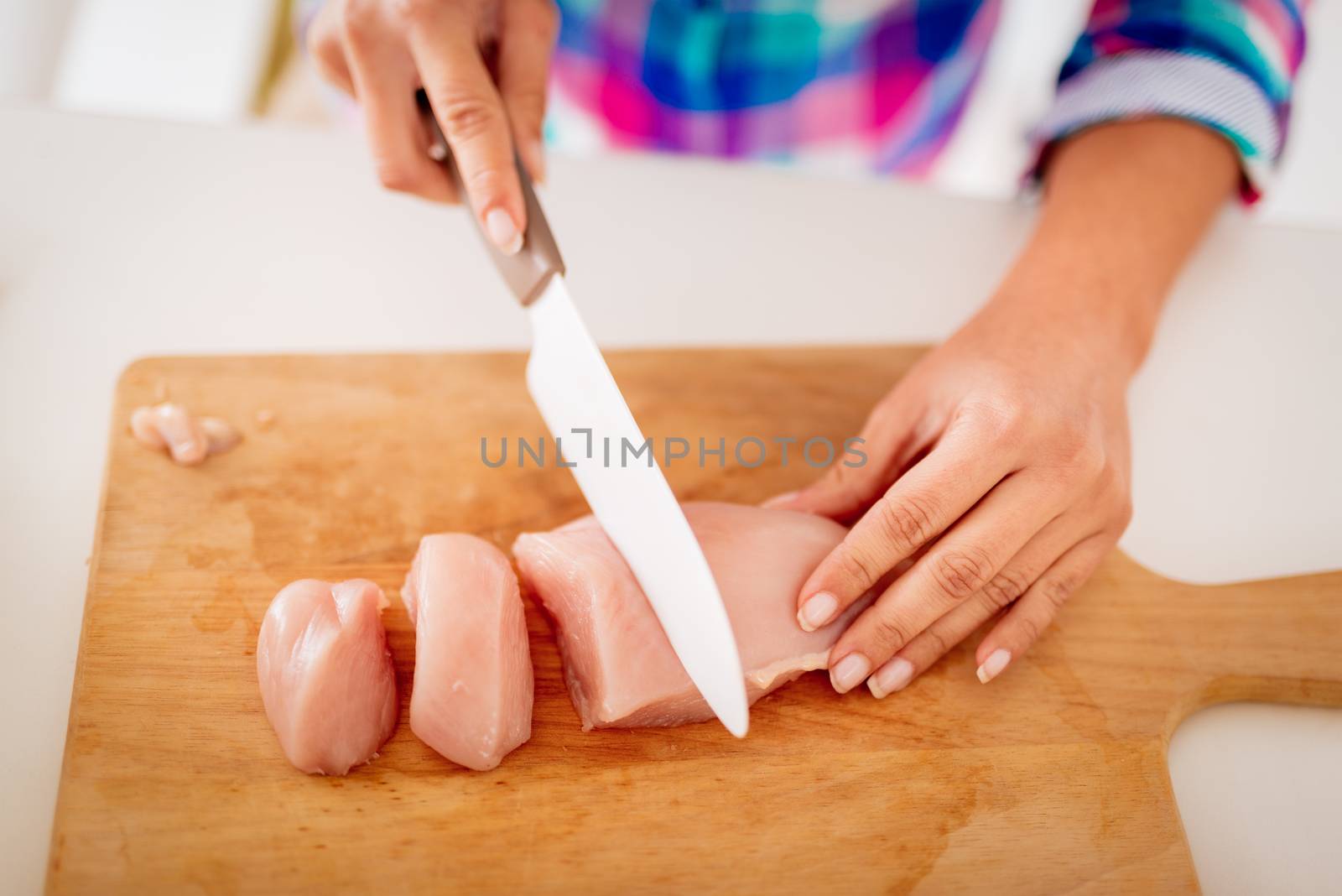 Close-up of a female hands cutting chicken filet on the kitchen board. Selective focus, focus on meat.
