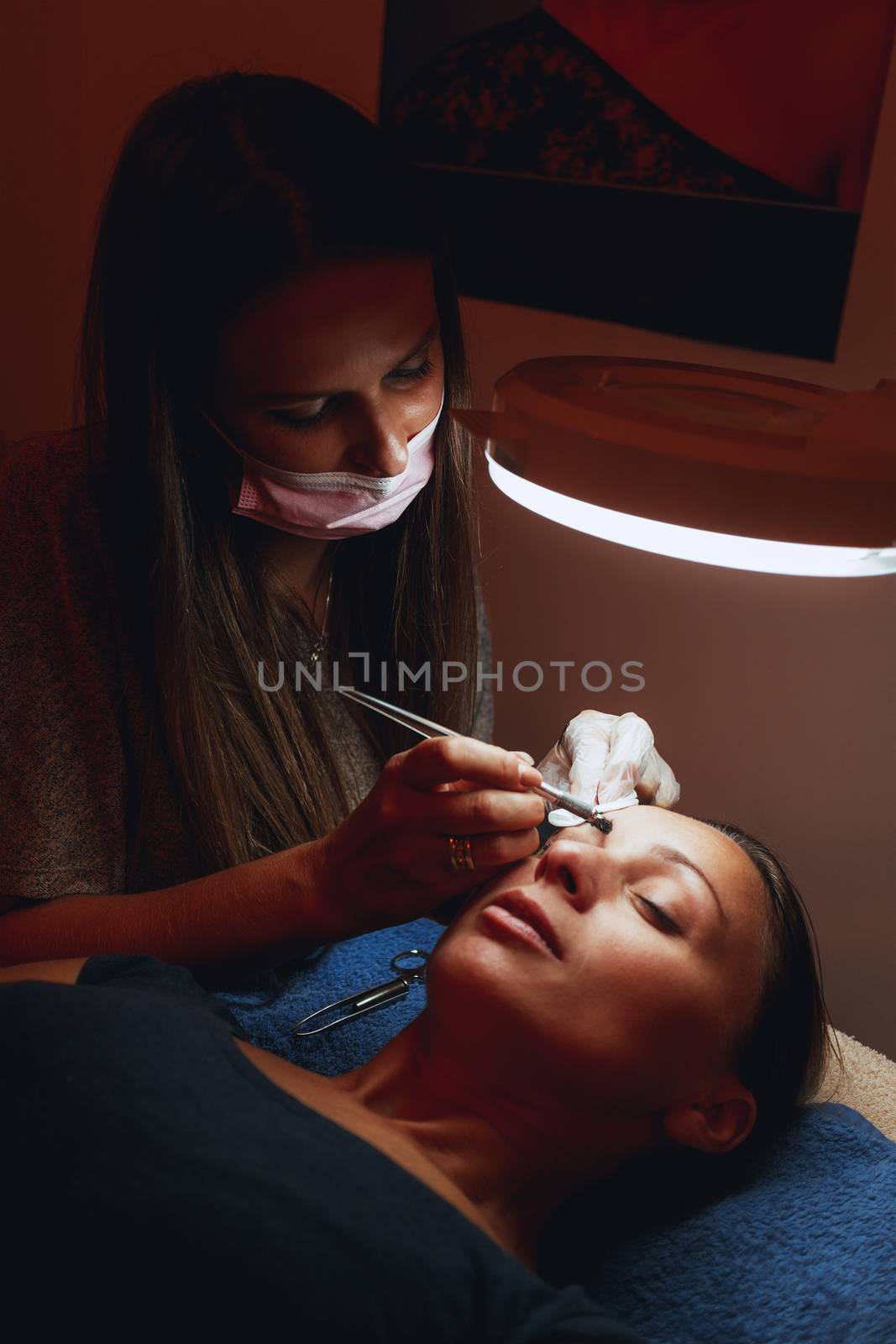 Beautician applying permanent makeup for eyebrows to model.  