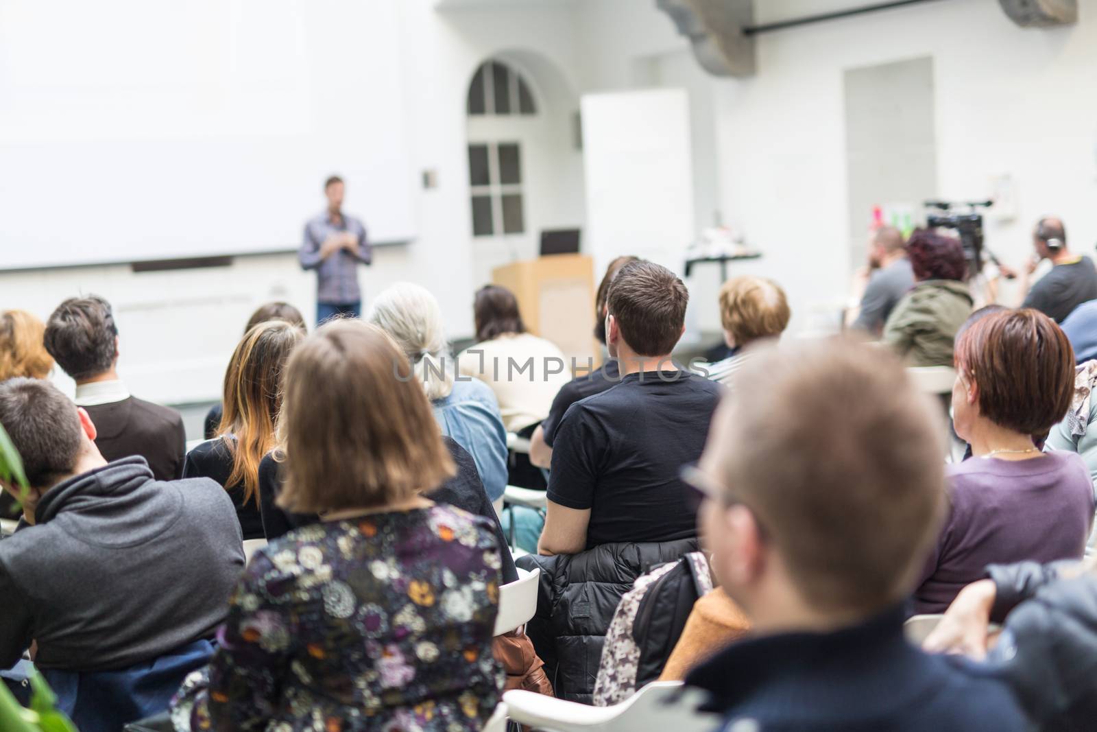 Male speaker giving presentation in lecture hall at university workshop. Audience in conference hall. Rear view of unrecognized participant in audience. Scientific conference event.
