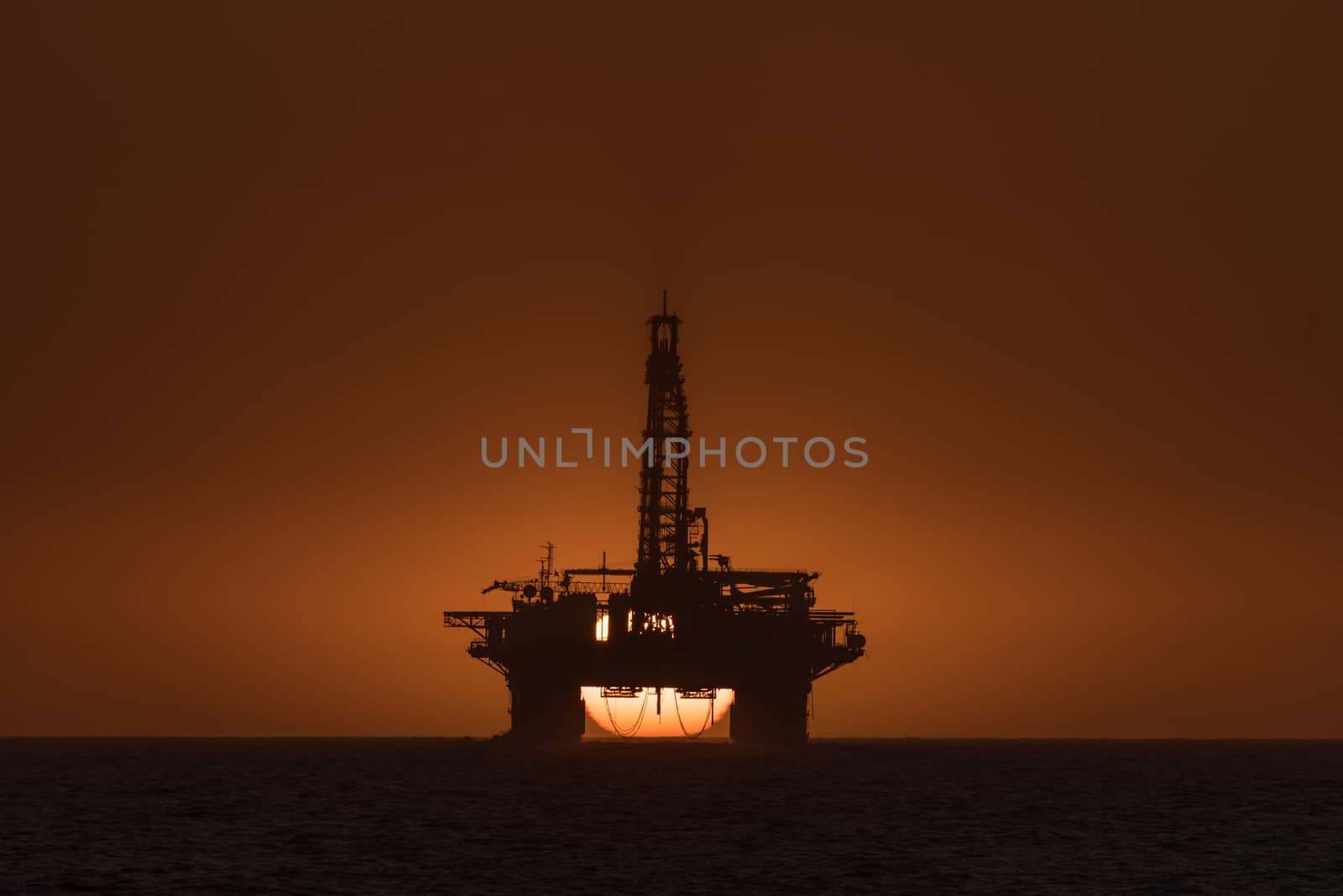 The sun is setting behind an oil drilling platform anchored in the Atlantic Ocean at Longbeach in the Namib Desert of Namibia