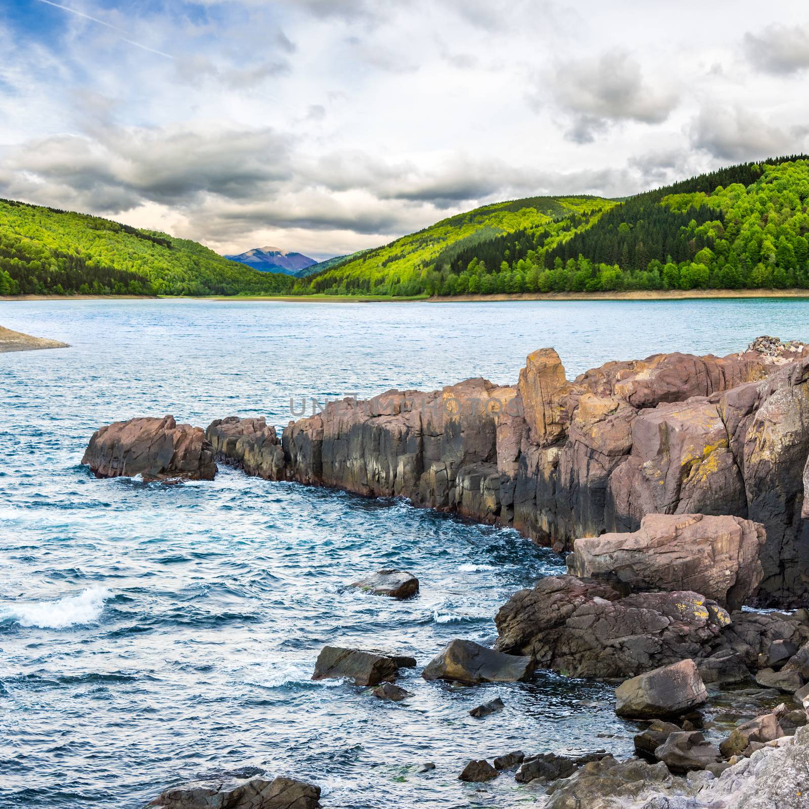 composite image of summer landscape  on lake with rocky shore and some boulders near forest in mountain  with high peak far away in morning light