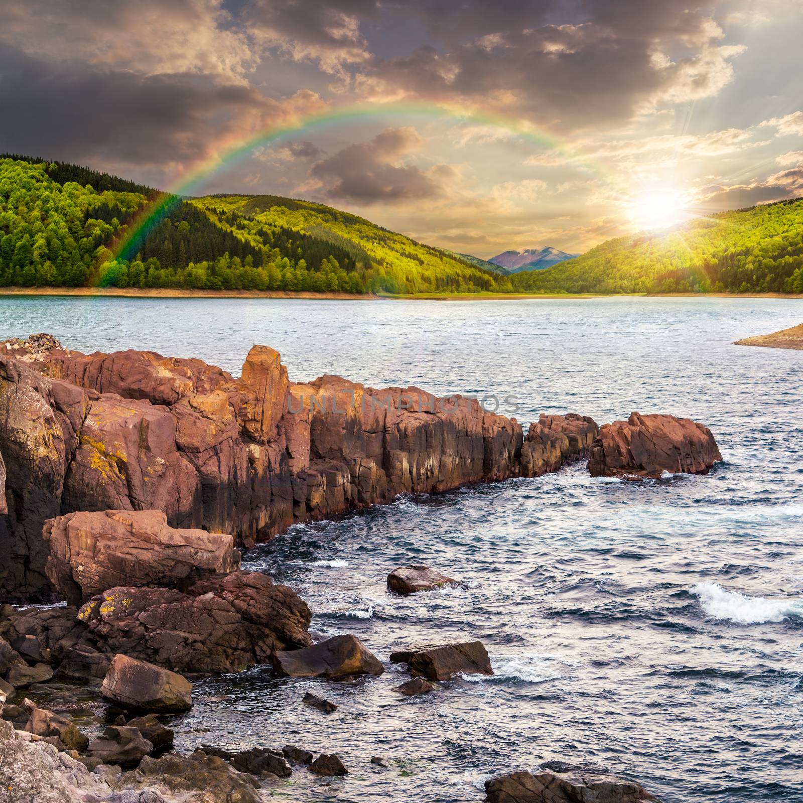 composite image of summer landscape  on lake with rocky shore and some boulders near forest under the rainbow  in mountain  with high peak far away in evening light