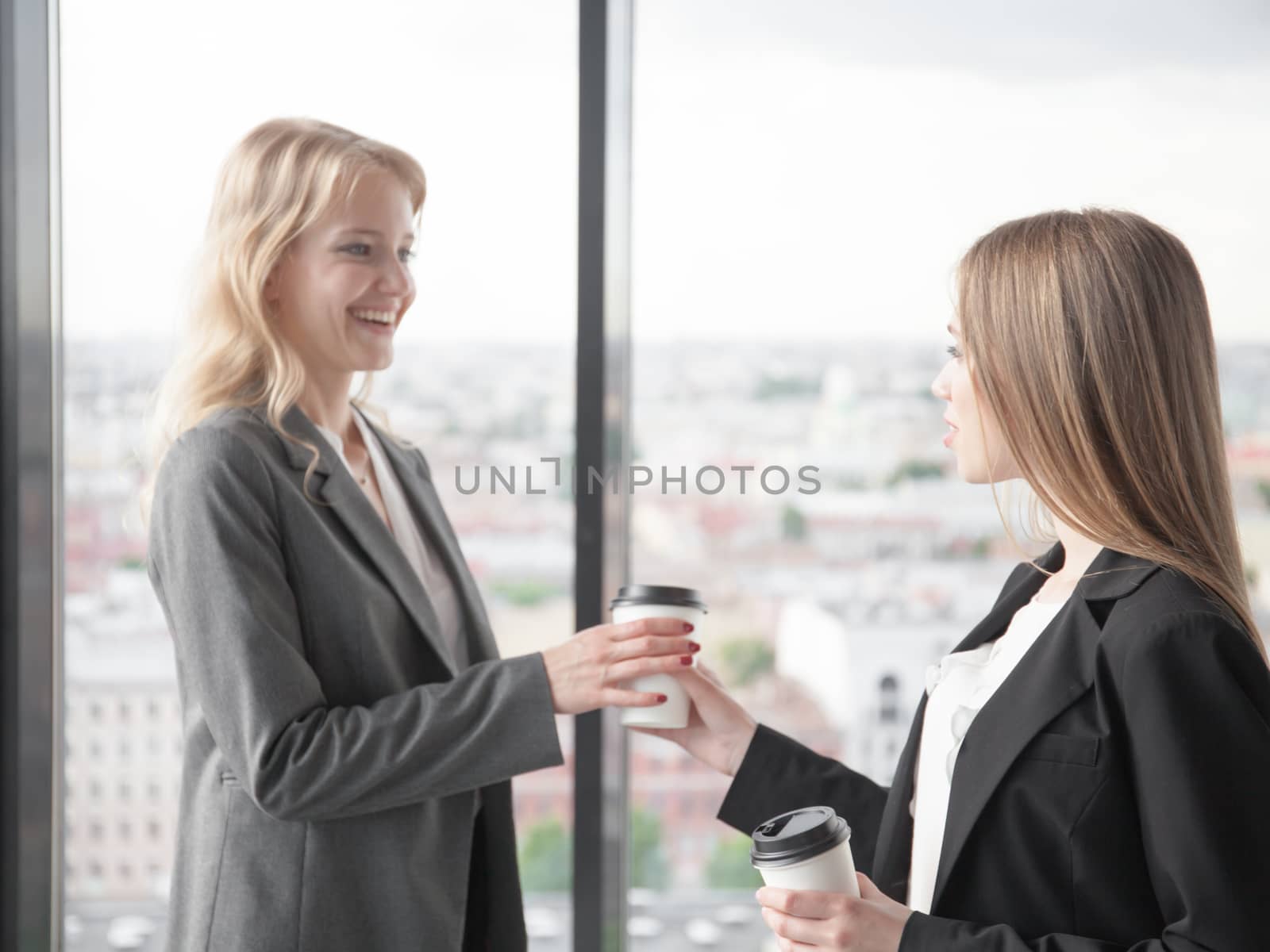 Business woman offering coffee to colleague in office with panoramic windows with view at city