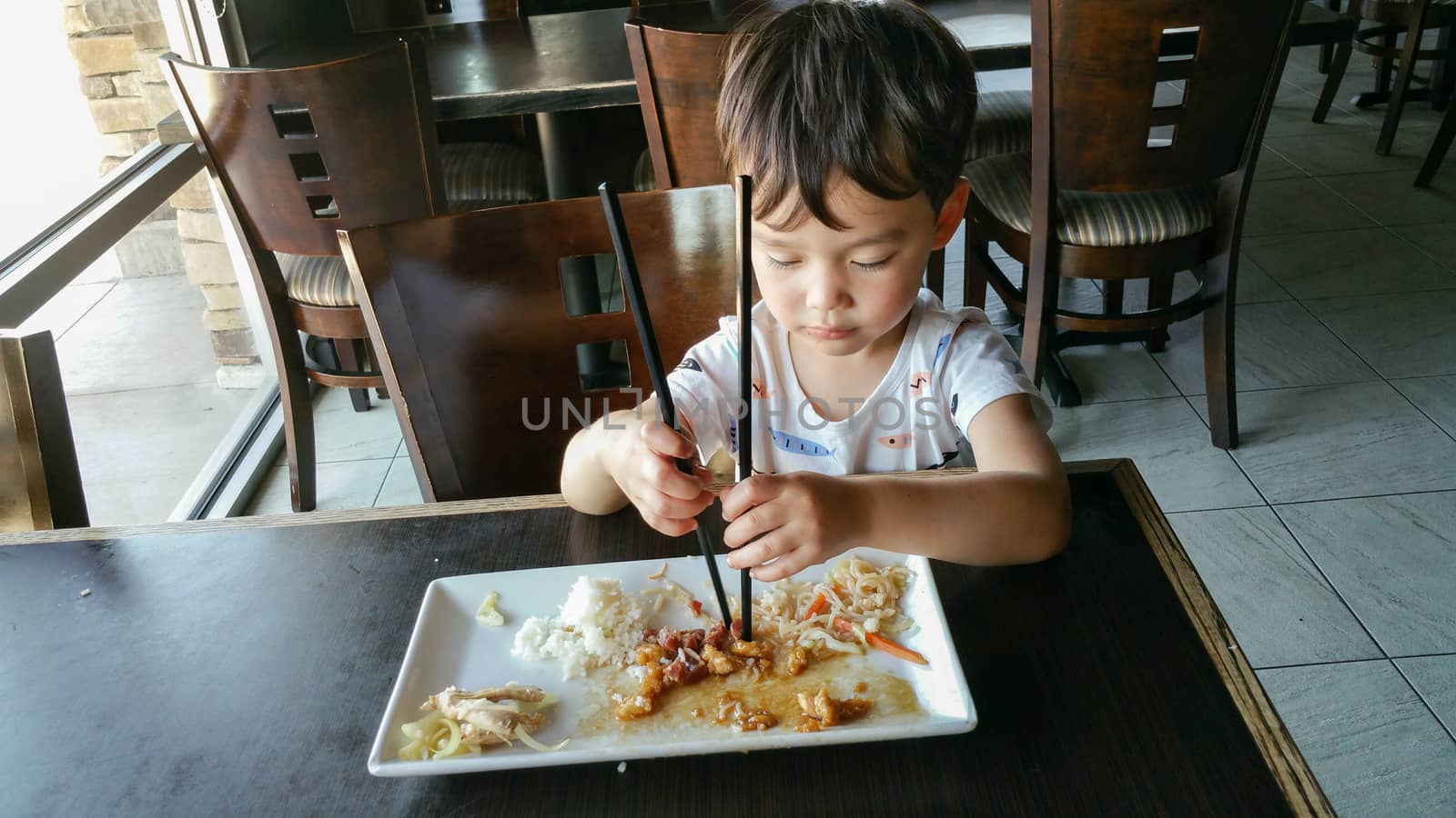 Cute Young Chinese and Caucasian Boy Learning To Use Chopsticks At Restaurant.