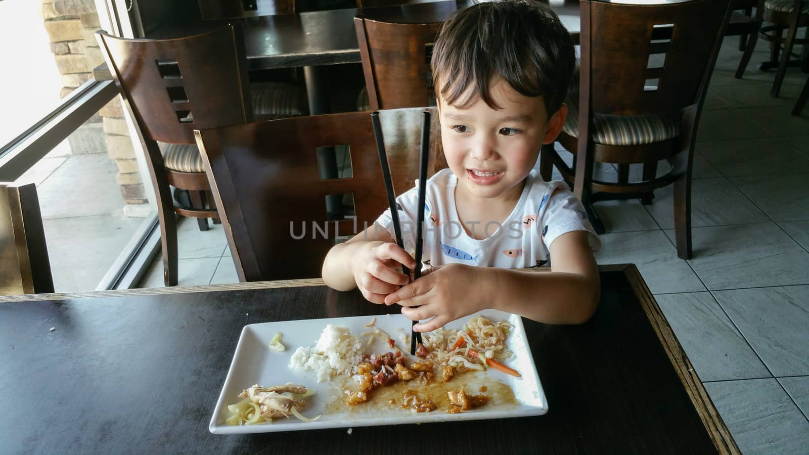 Cute Young Chinese and Caucasian Boy Learning To Use Chopsticks At Restaurant.