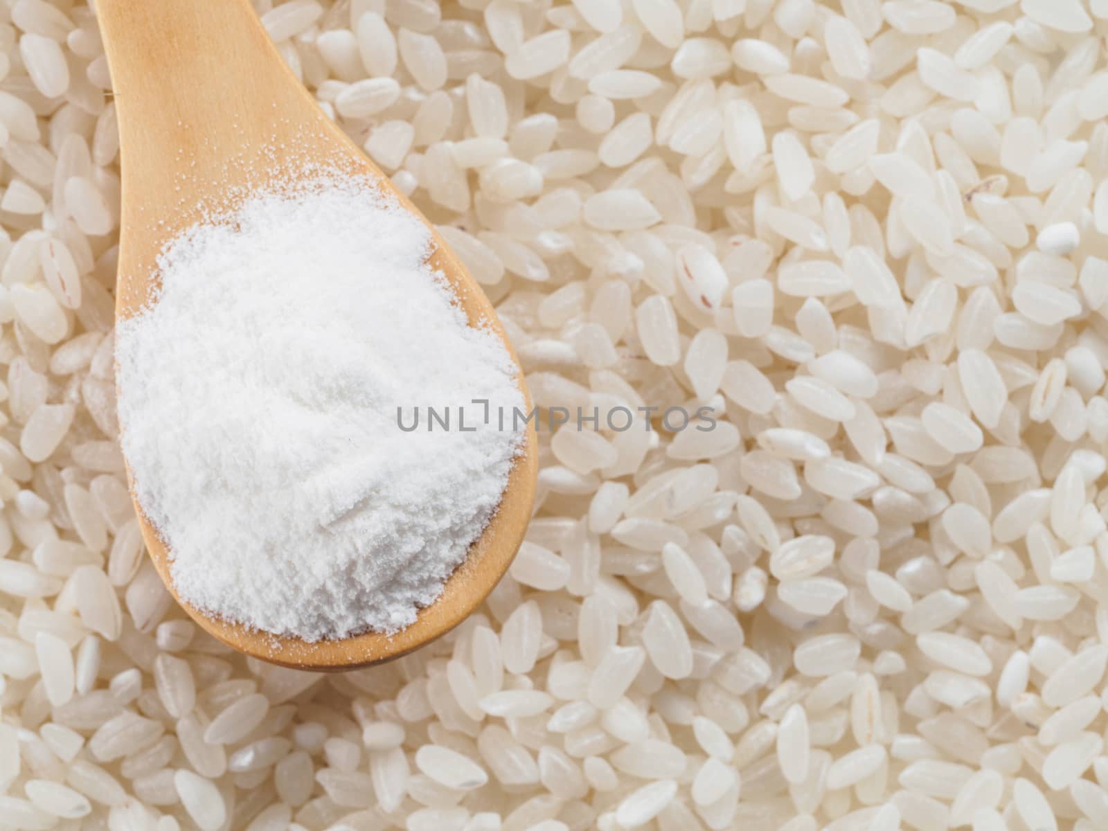 rice flour in wooden spoon and rice grains. whole-grain rice flour on rice grains background. Copy space. Top view or flat lay.