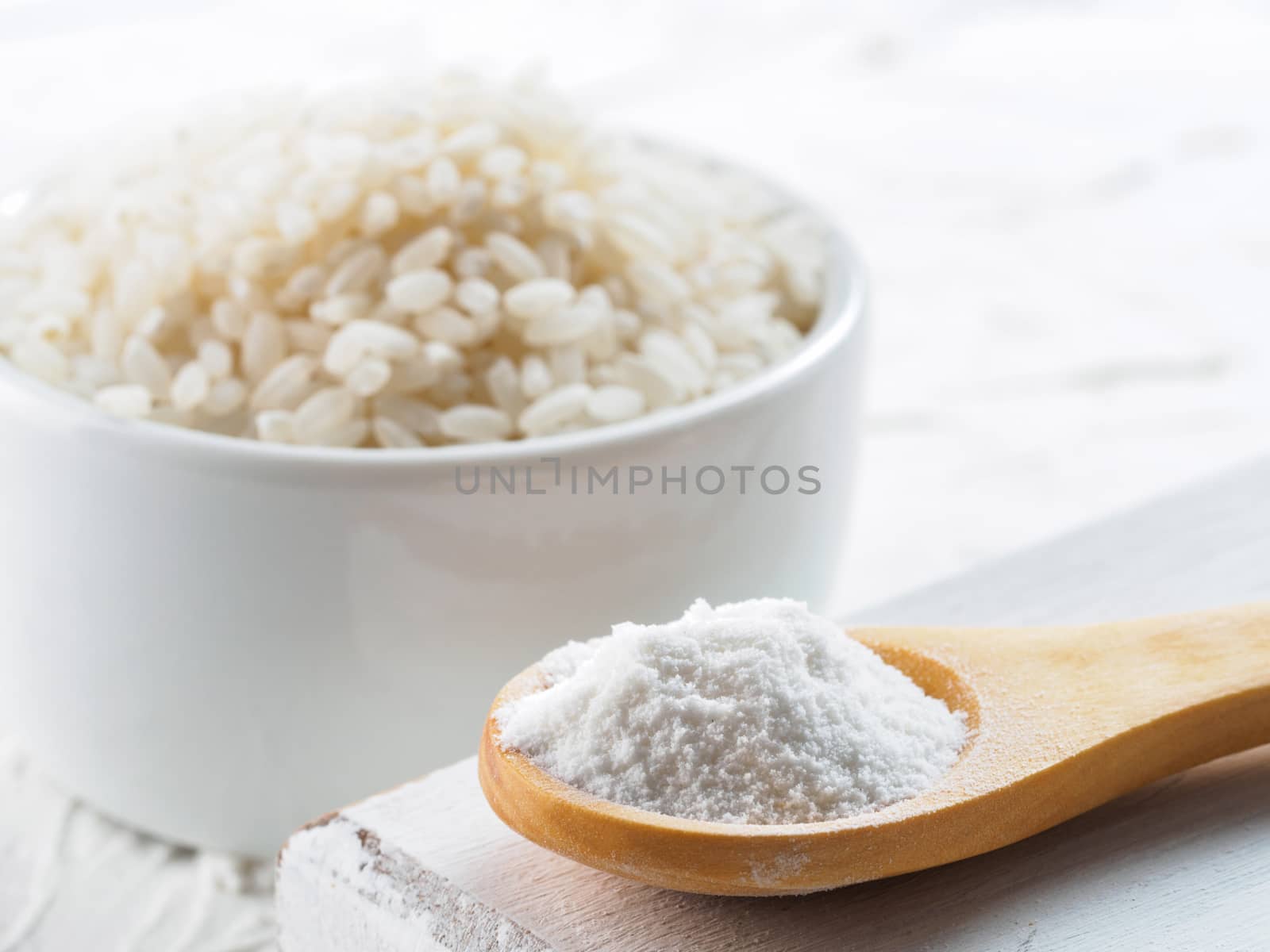 rice flour in wooden spoon and rice grains on white background