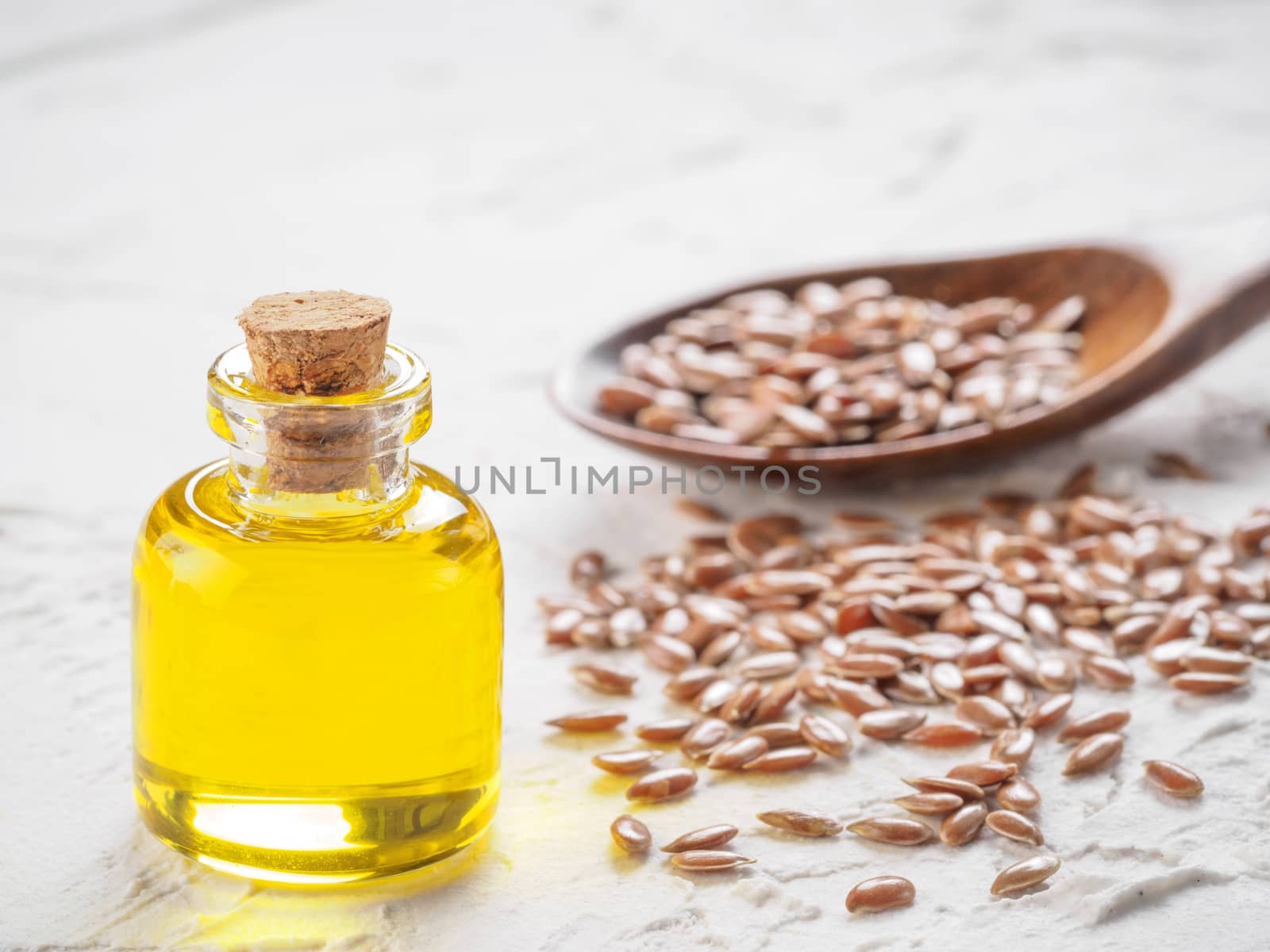 Brown flax seeds in spoon and flaxseed oil in glass bottle on white concrete background. Flax oil is rich in omega-3 fatty acid. Copy space.
