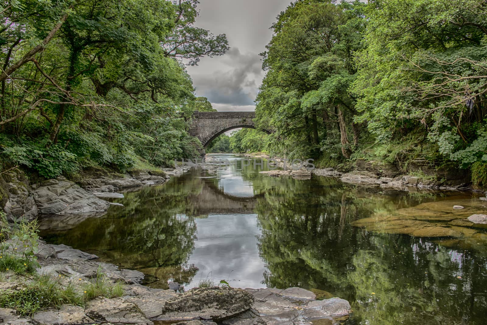 A view down a river with a bridge spanning it and with reflections in the water. A typical british country scene