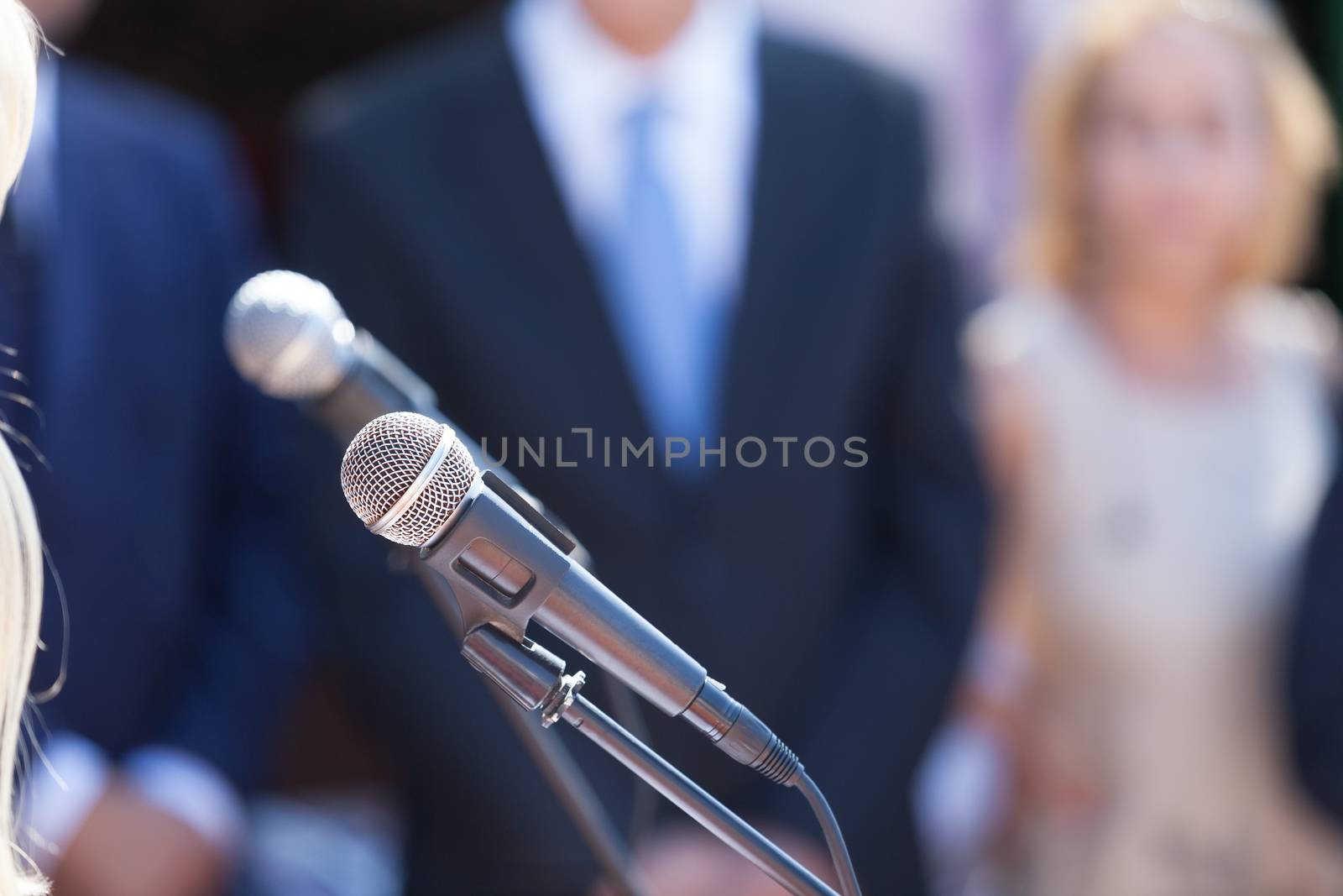 Press conference. Microphone in focus against blurred group of people.