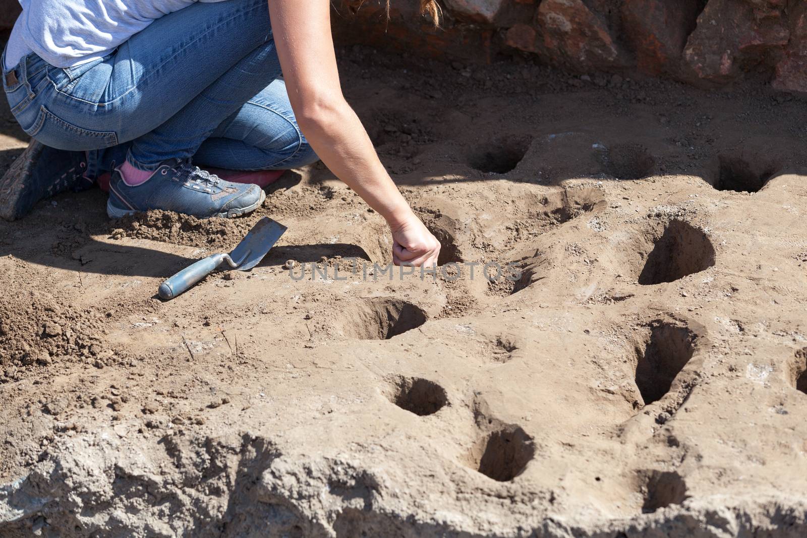 Female archaeologist digging holes at archaeological site
