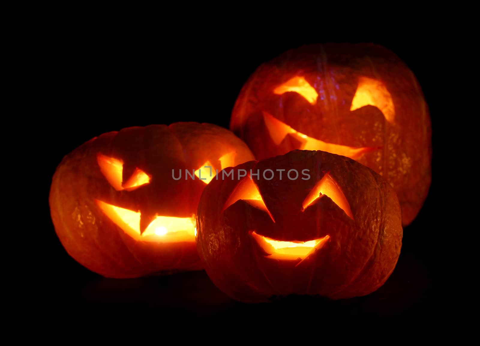 Illuminated cute three halloween pumpkins isolated on black background