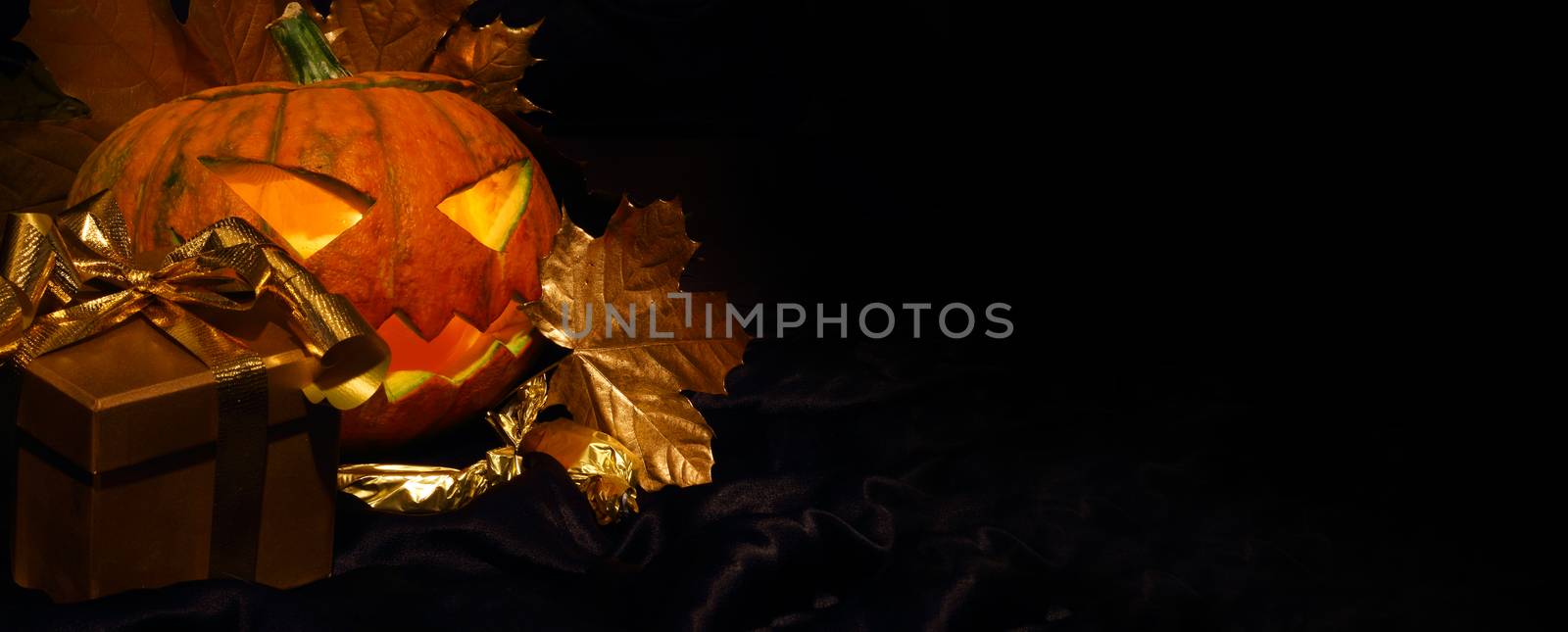 Halloween pumpkin with autumn leafs and gift on black