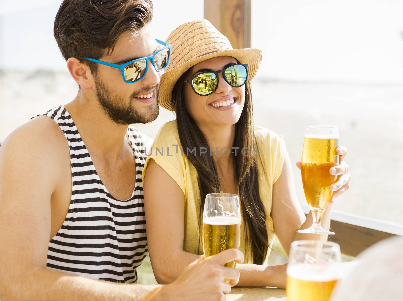 Friends having fun and drinking a cold beer at the beach bar