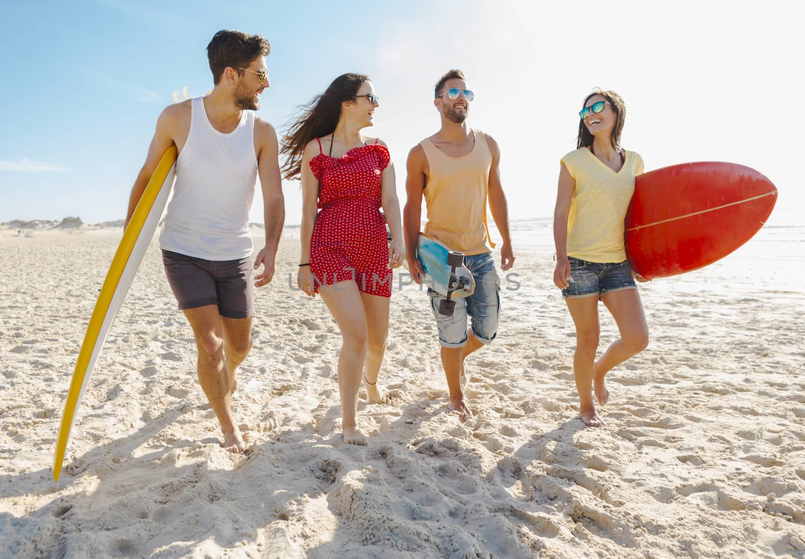 Friends walking together at the beach and holding surfboards