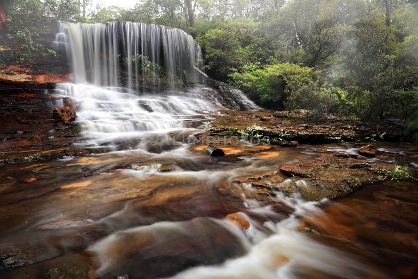 Weeping rock, a tranquil lush waterfall, seen here spilling over and flowing downstream. Blue Mountains Australia