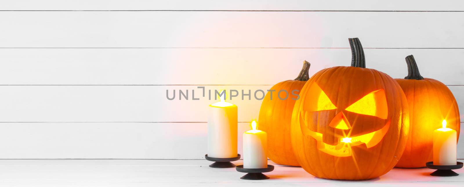 Halloween pumpkin head jack lantern and candles on white wooden background