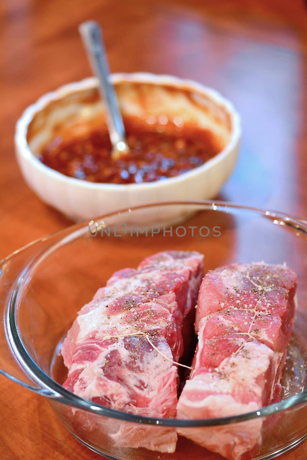 Two pieces of raw pork necks and bowl with spicy marinade on a desk.