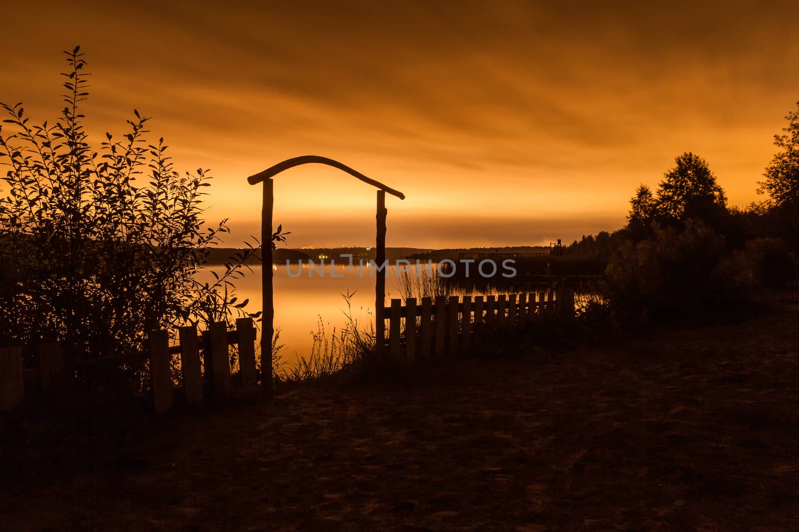 Night landscape. A fence before a pond and the night city on the horizon