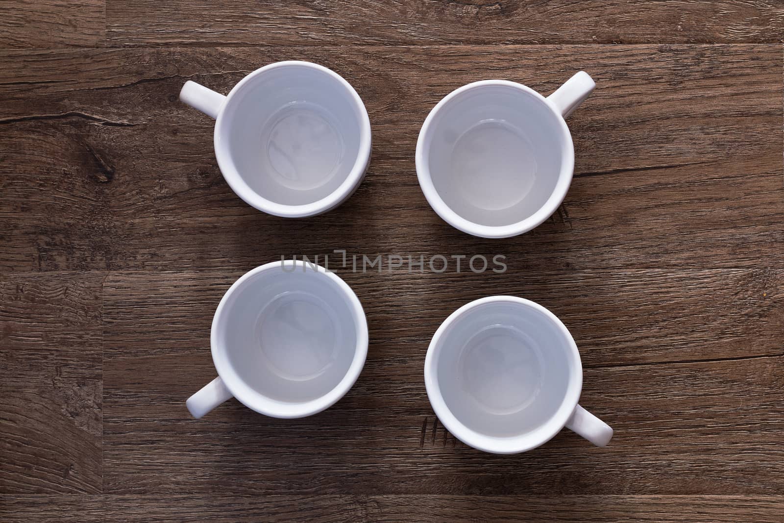 Food concept - top view of four white cups without saucers on gray brown wood table. Empty ceramic mugs