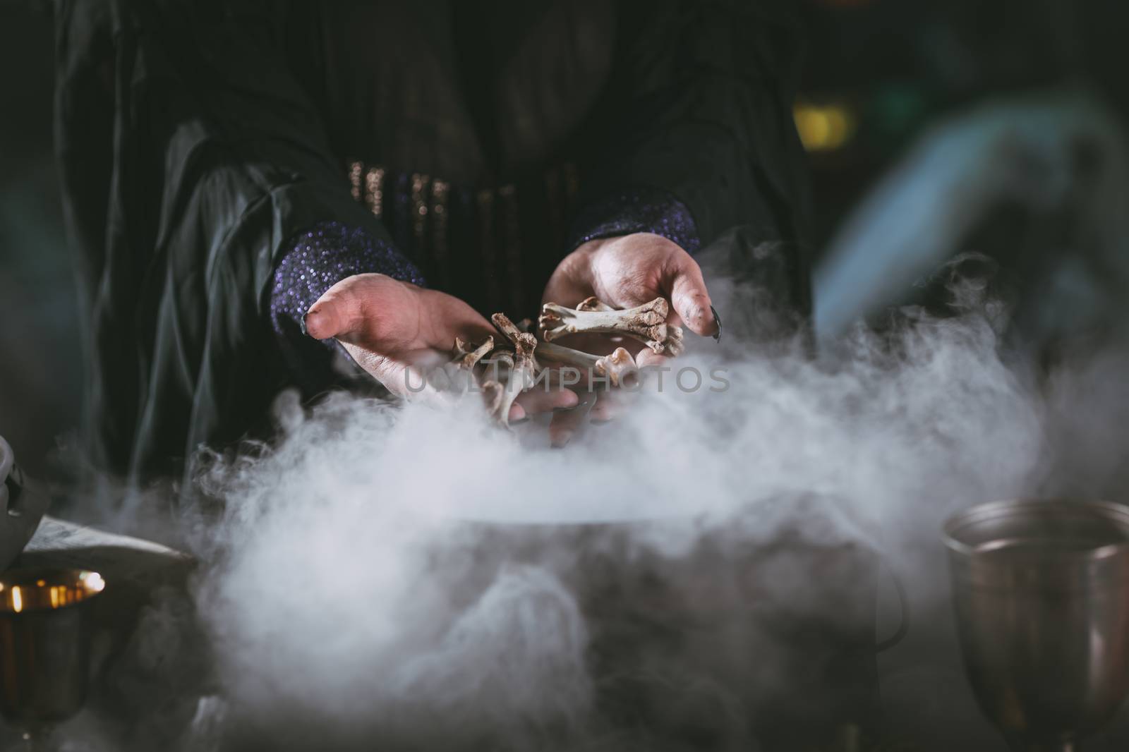 Close-up of a witches hands holding bones above boiling water for a cooking poison soup.