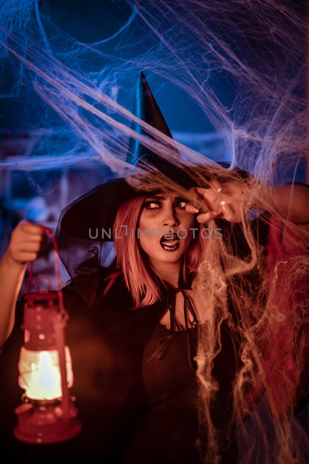 Witch with lighted lantern in her hand in creepy cobweb surroundings is looking for saomething.