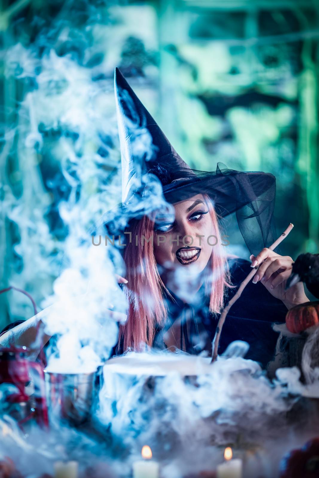 Witch with smiling face in creepy surroundings cooks poison soup in boiling cauldron.