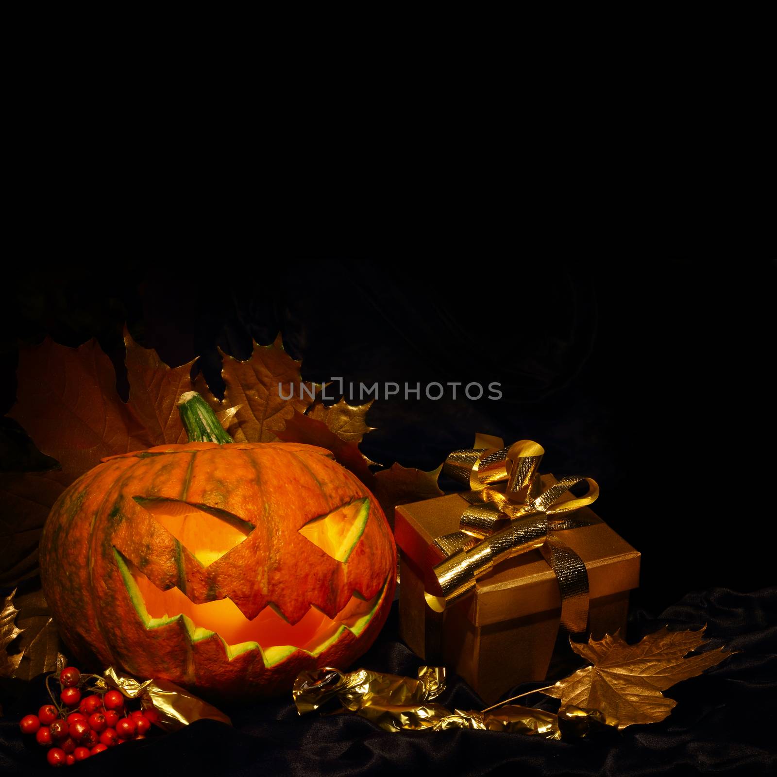 Halloween pumpkin with autumn leafs and gift on black
