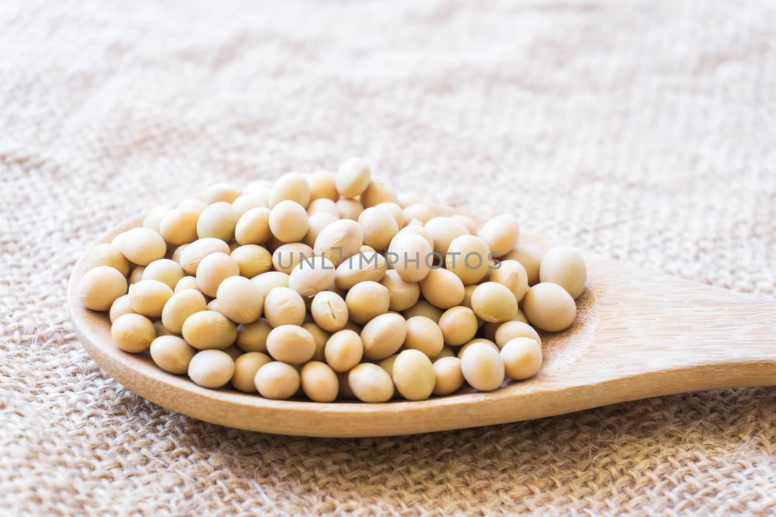 Closeup soy beans on wood spoon with sackcloth background , healthy food concept