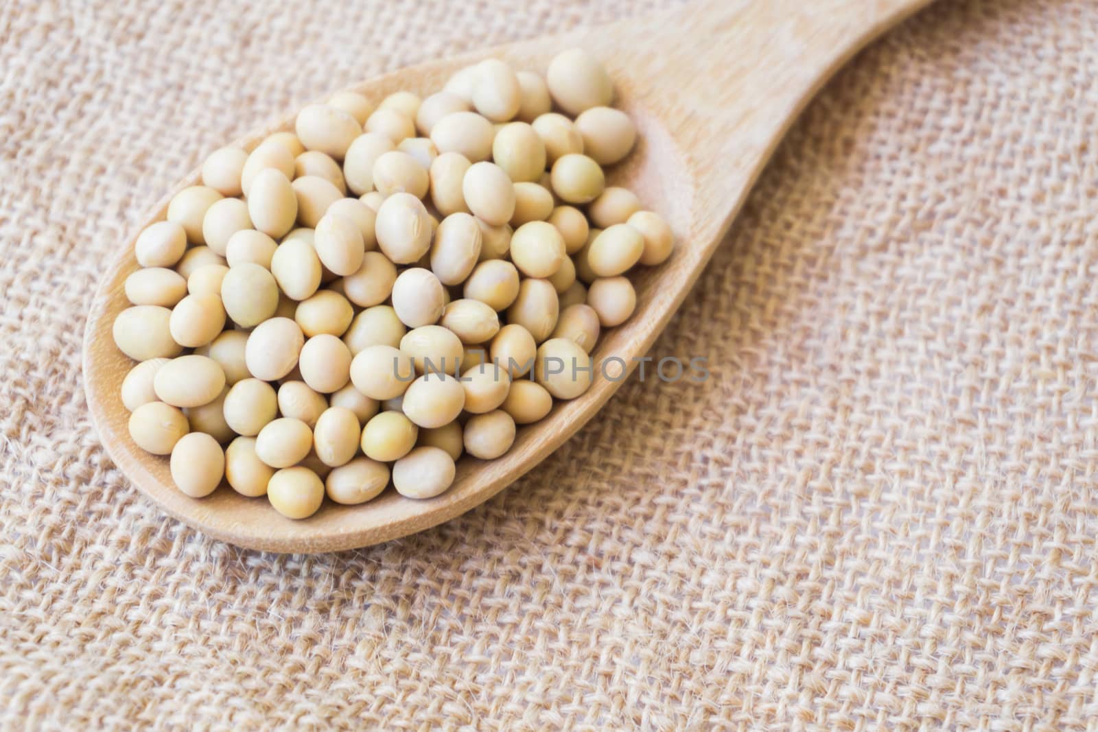 Closeup soy beans on wood spoon with sackcloth background , healthy food concept