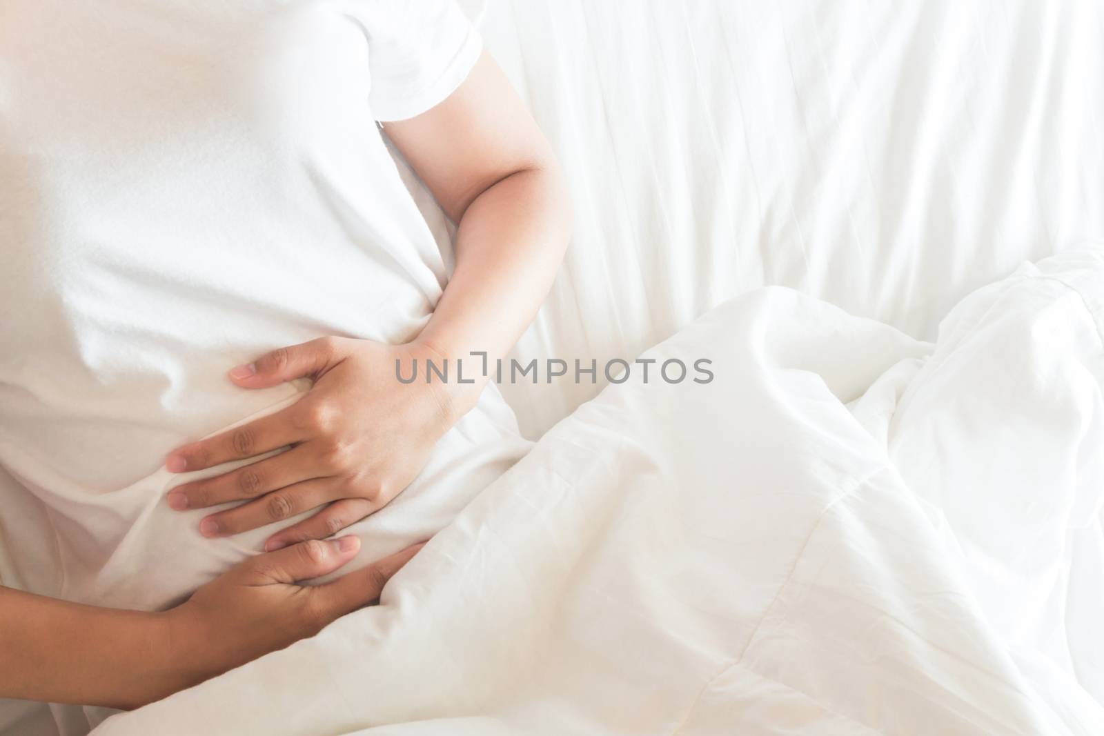 Closeup woman hand holding abdominal with stomach ache lying on bed, health care and medical concept