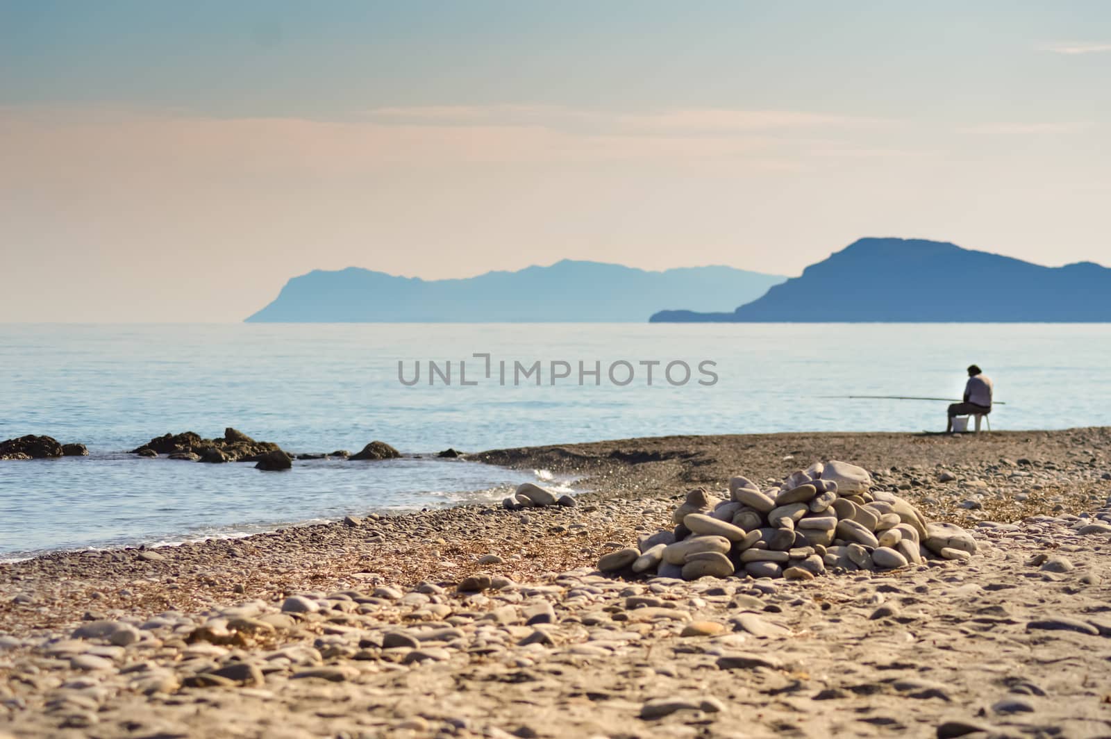 Solitary fisherman sitting on the pebble beach of Maleme facing the mountains