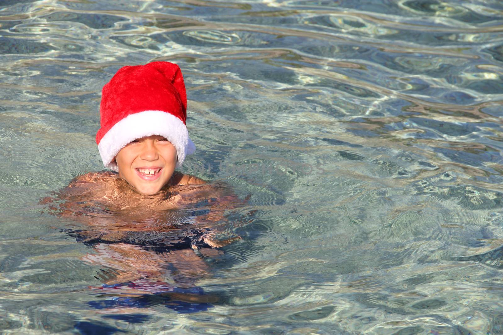 Smiling boy in Santa hat in sea by destillat