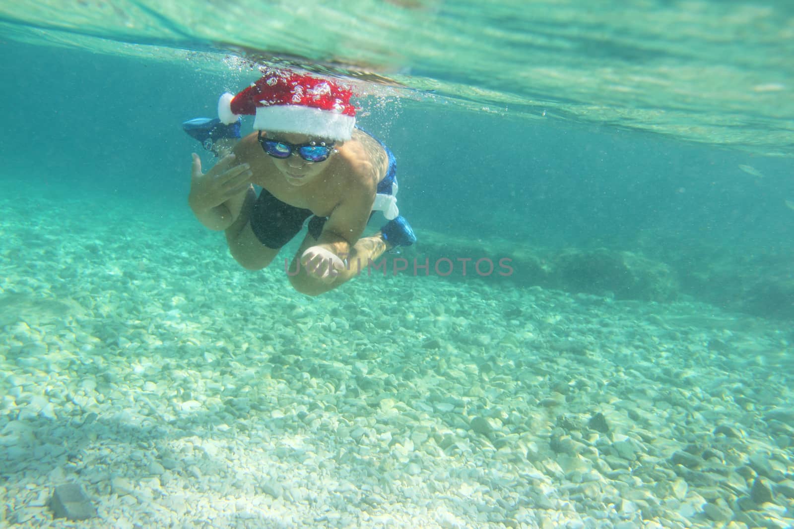 Boy in Santa hat swimming in sea by destillat
