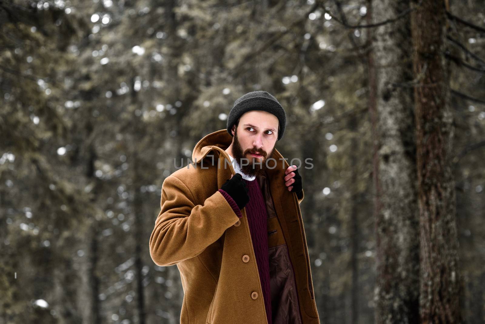 man in the winter forest is cold and in a brown coat and gloves