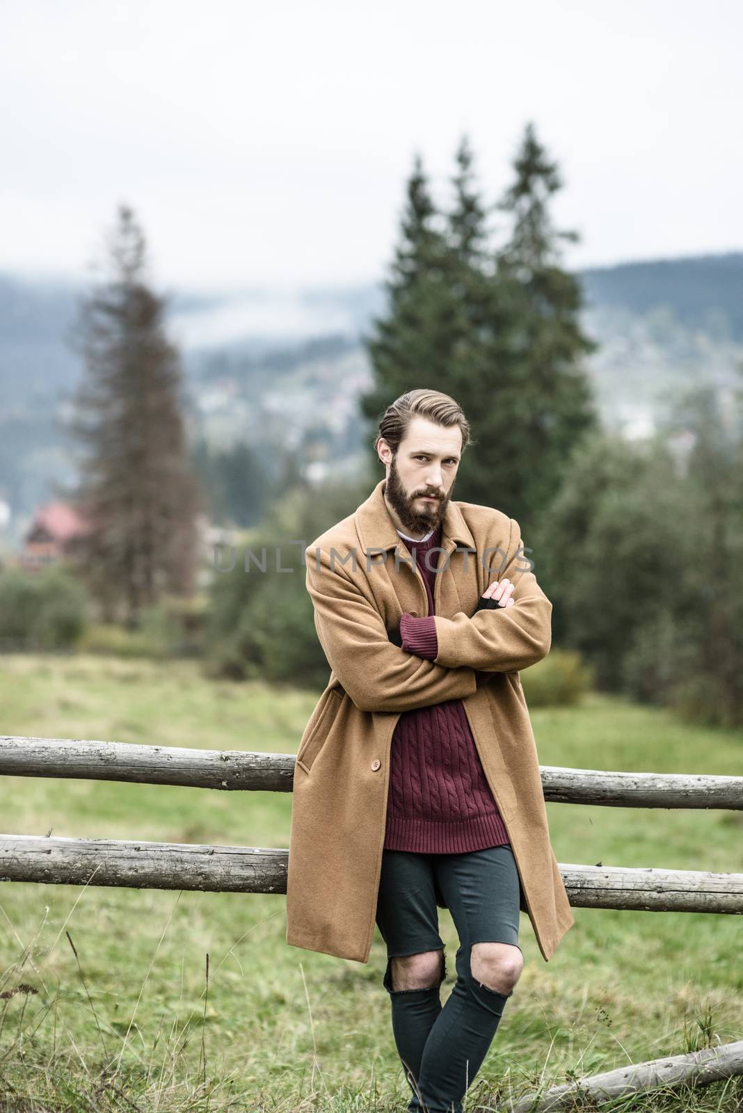 man in a brown coat and torn trousers was leaning against the fence