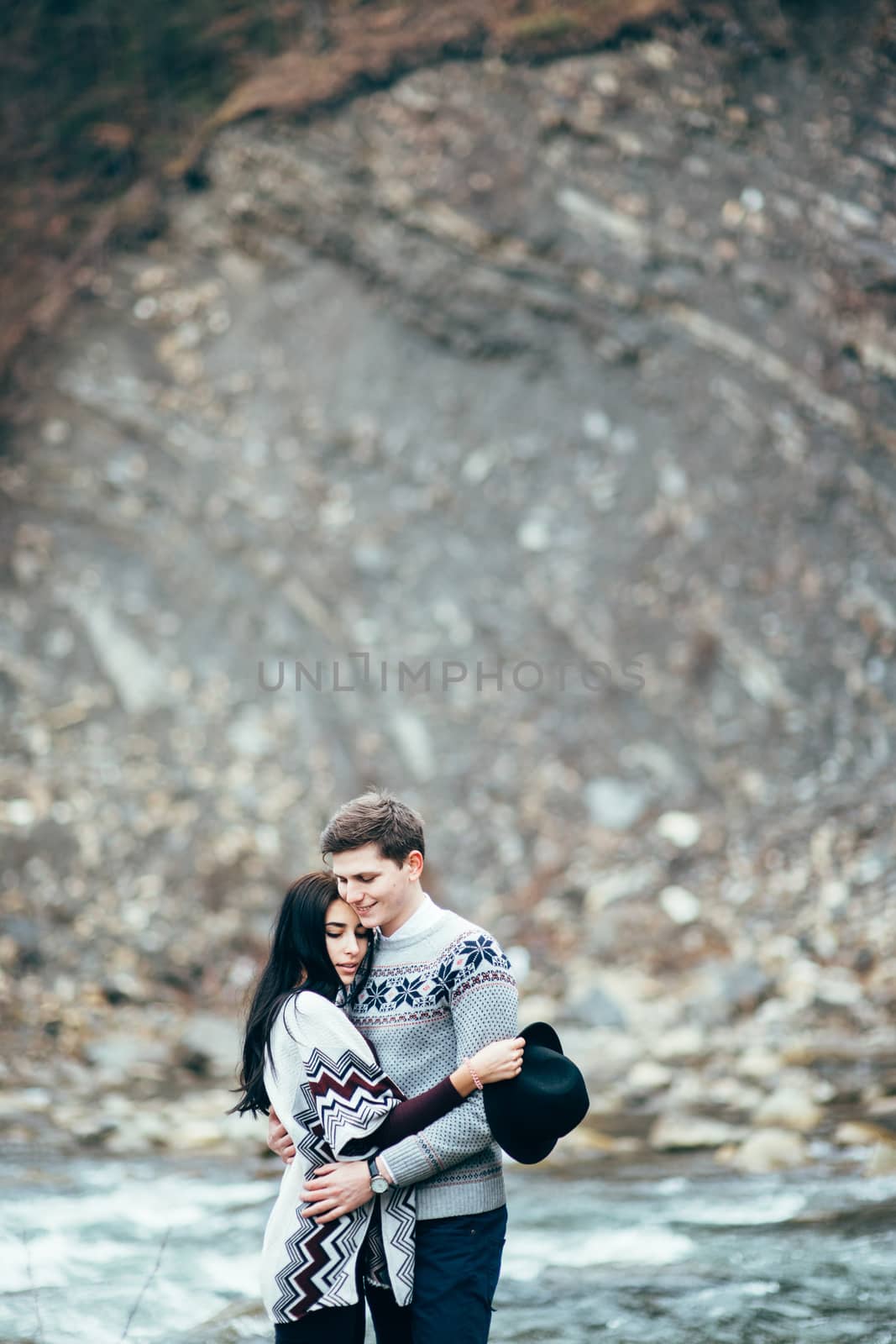 guy and girl in warm sweaters walking along a mountain river, love story