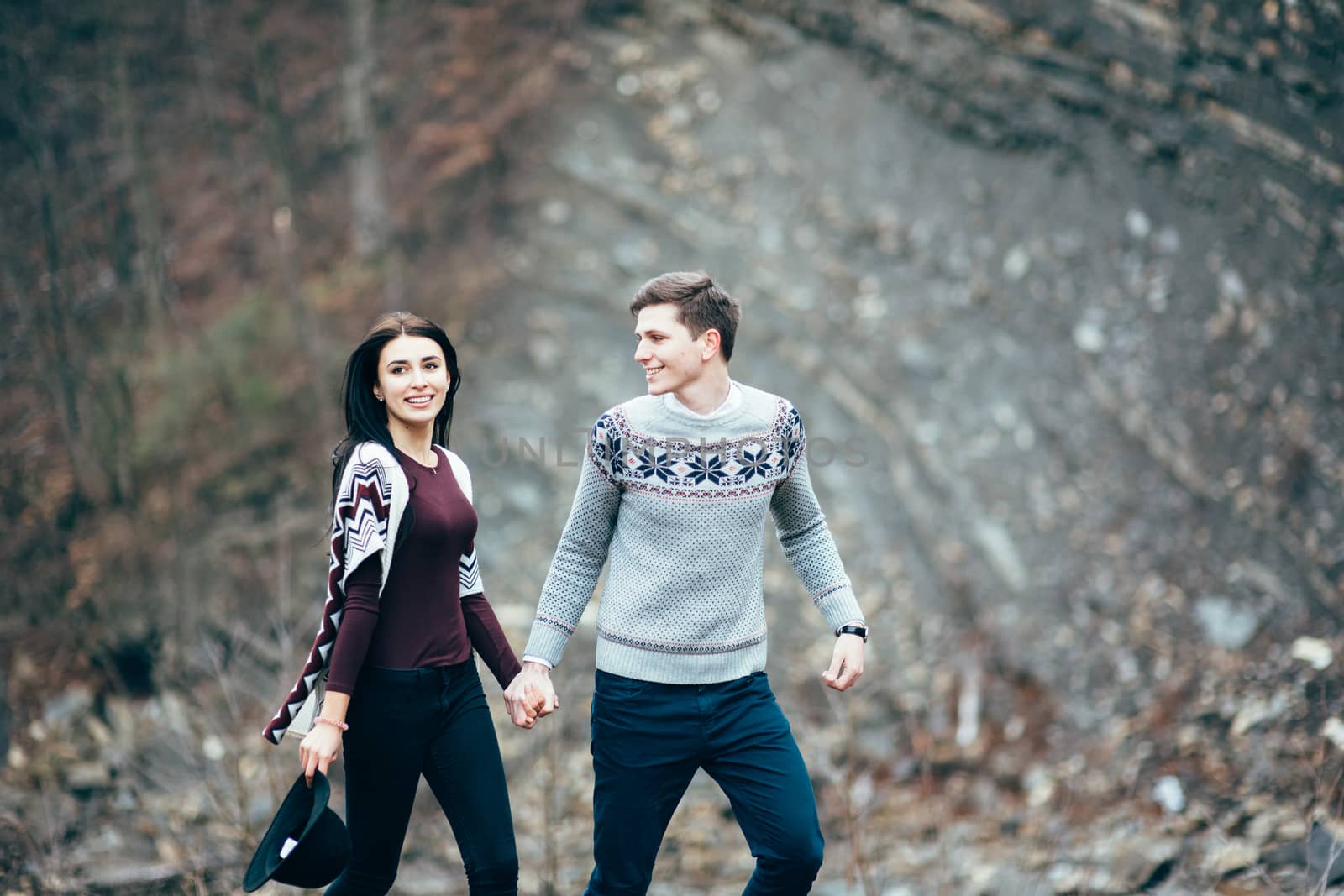 guy and girl in warm sweaters walking along a mountain river, love story