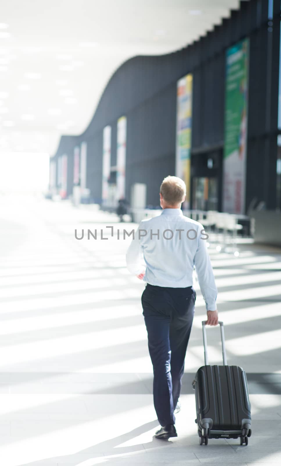 Business man in formal clothing walking with wheeled bag at airport terminal