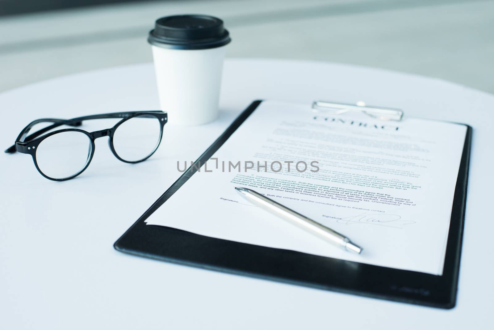 A pair of women's glasses and a pen lying on top of a white sheet of paper on wooden surface. The sheet has a coffee stain. Copy space in lower and right part of image. High angle view. by ALotOfPeople