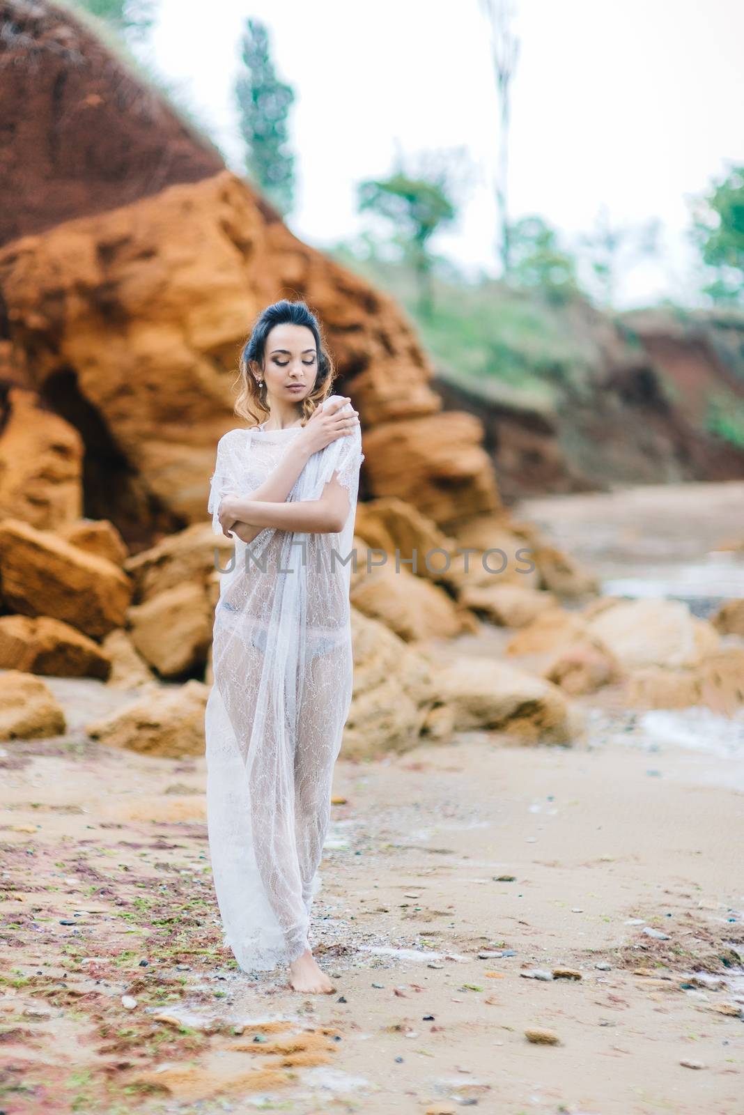 bride in her underwear and a dressing gown with a veil walks on the beach