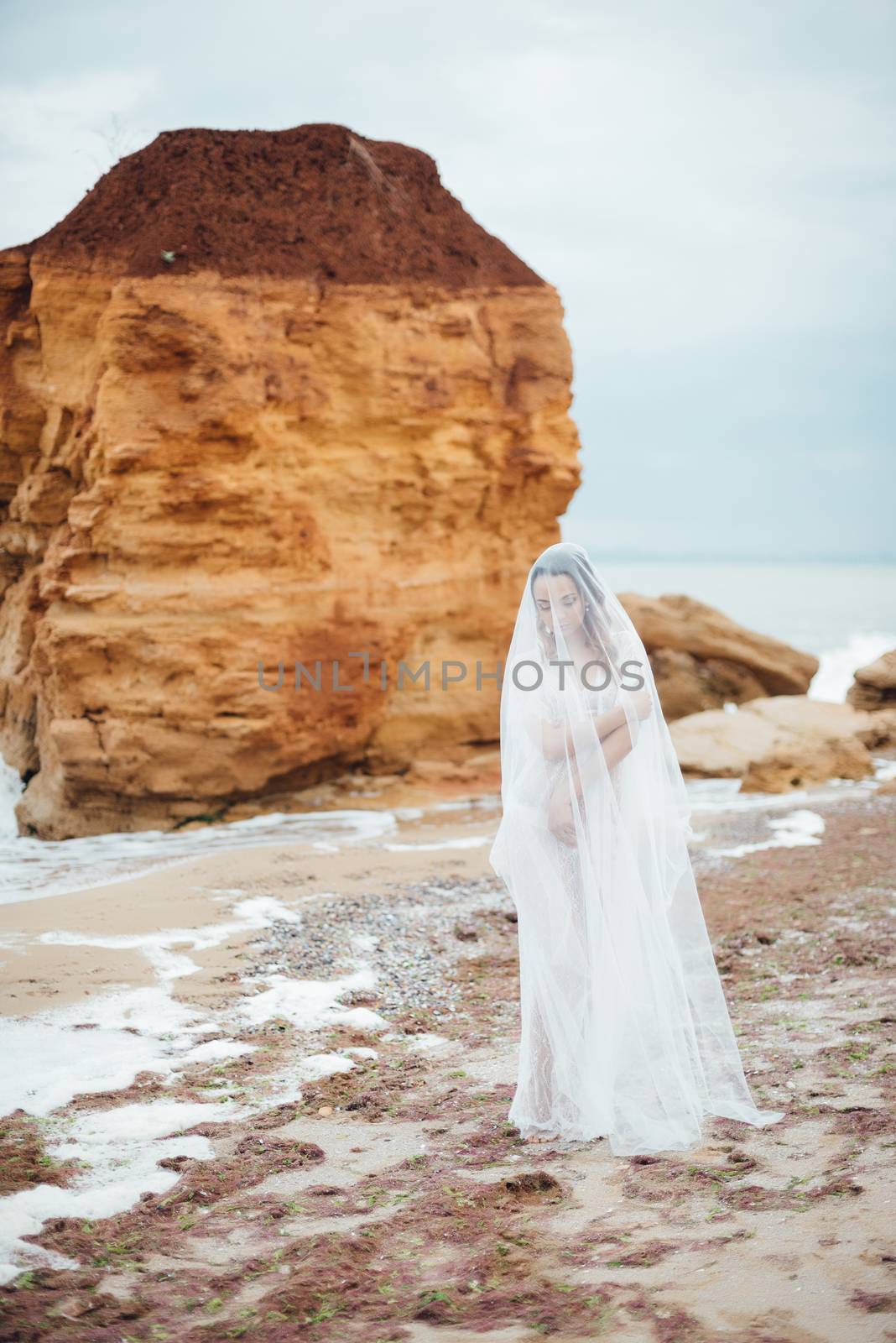 bride in her underwear and a dressing gown with a veil walks on the beach