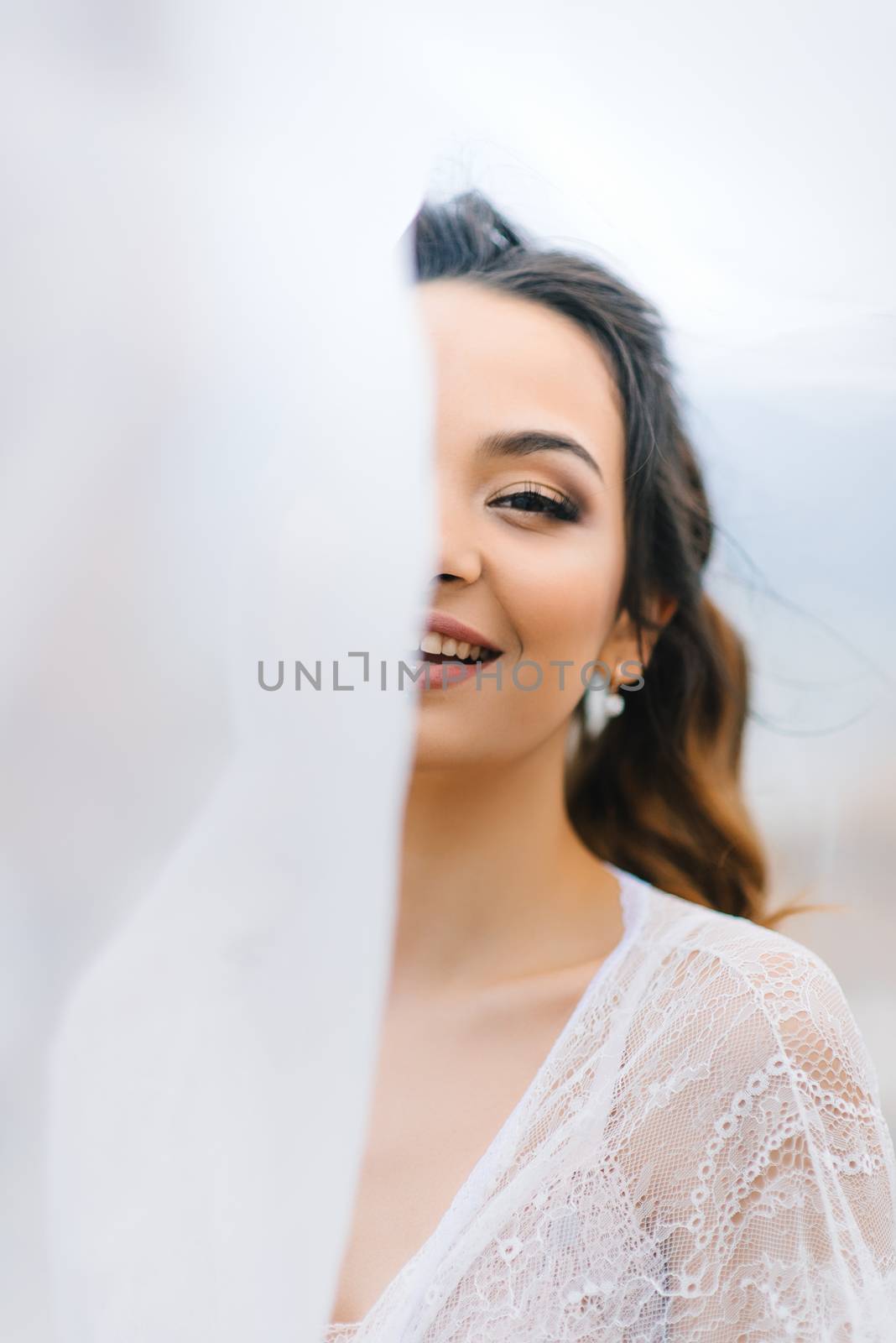 bride in her underwear and a dressing gown with a veil walks on the beach