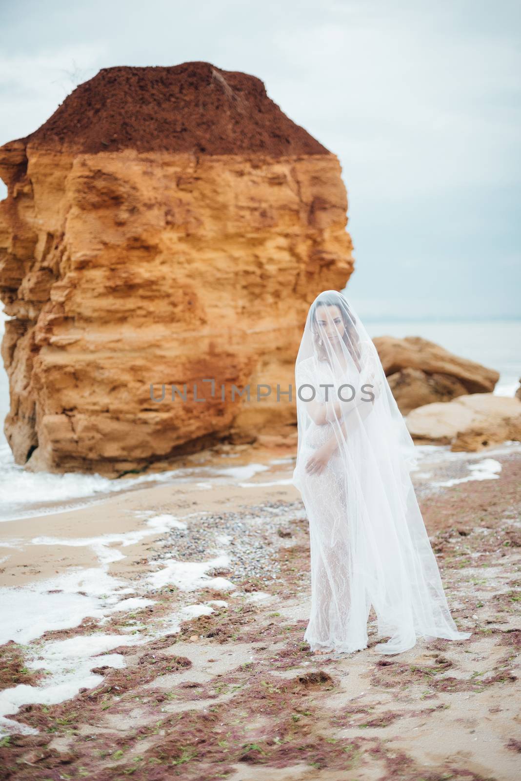 bride in her underwear and a dressing gown with a veil walks on the beach