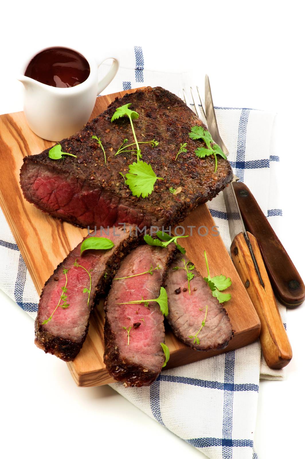 Delicious Sliced Roast Beef Medium Rare on Cutting Board with Tomato Sauce, Fork and Table Knife on Checkered Napkin closeup on White background