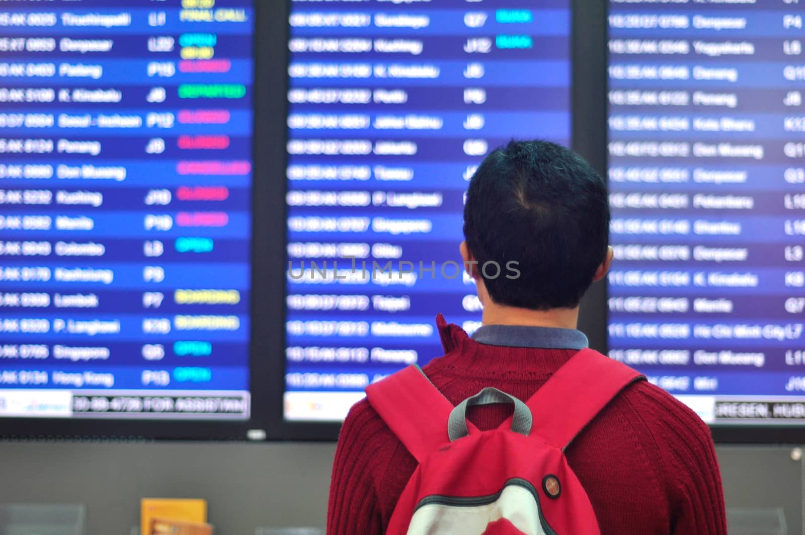 Young man with backpack in airport near flight timetable.