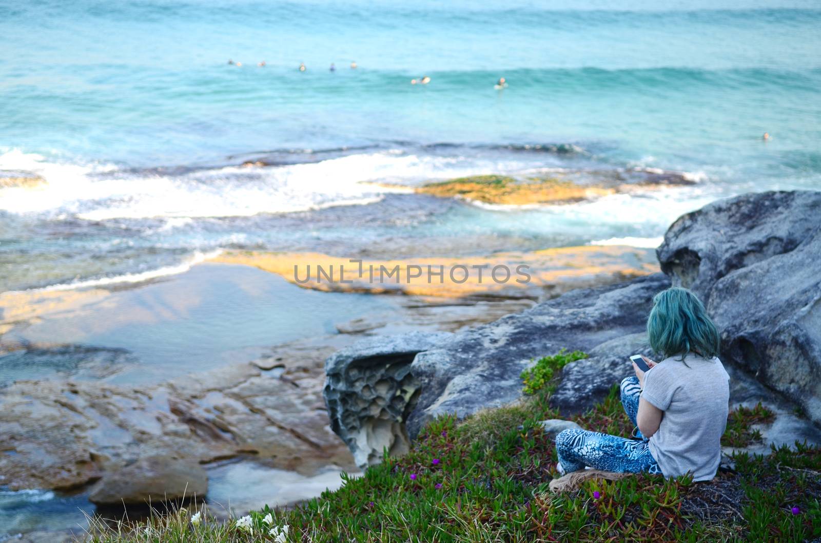 Travel girl sitting on top of a  cliff along the Bondi to Coogee coastal walk in Sydney, Australia. Back view young female relaxing along the beach.