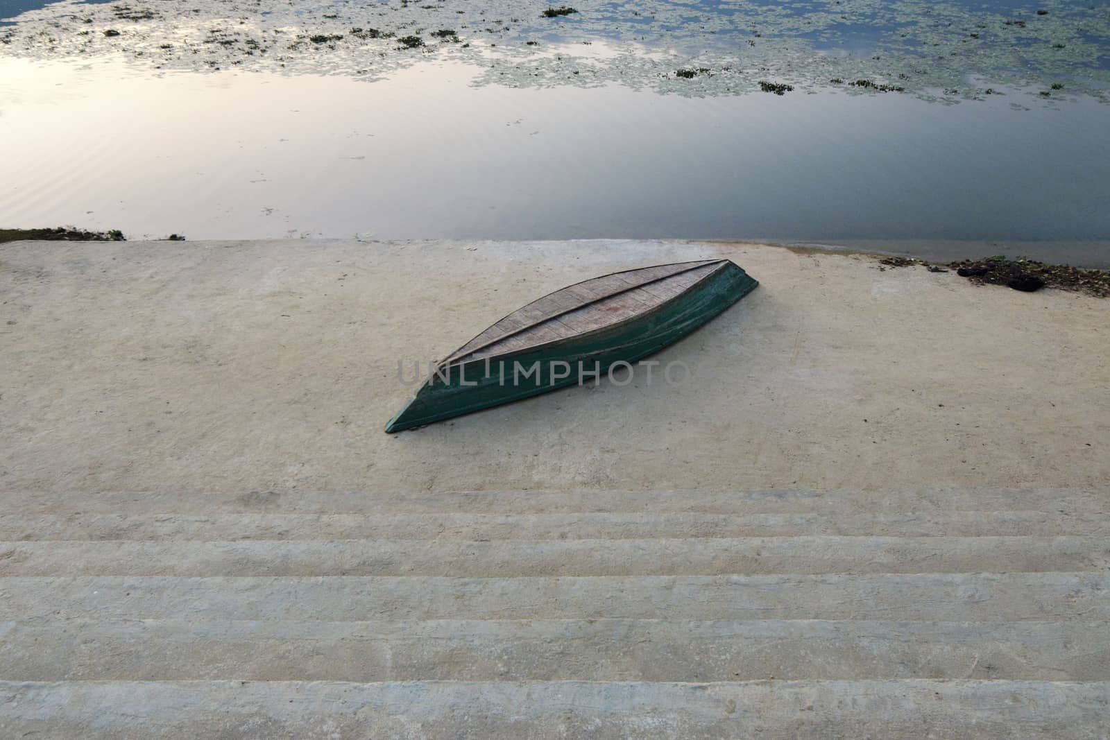 An inverted boat on a concrete embankment on the shore of a mountain lake at sunset.