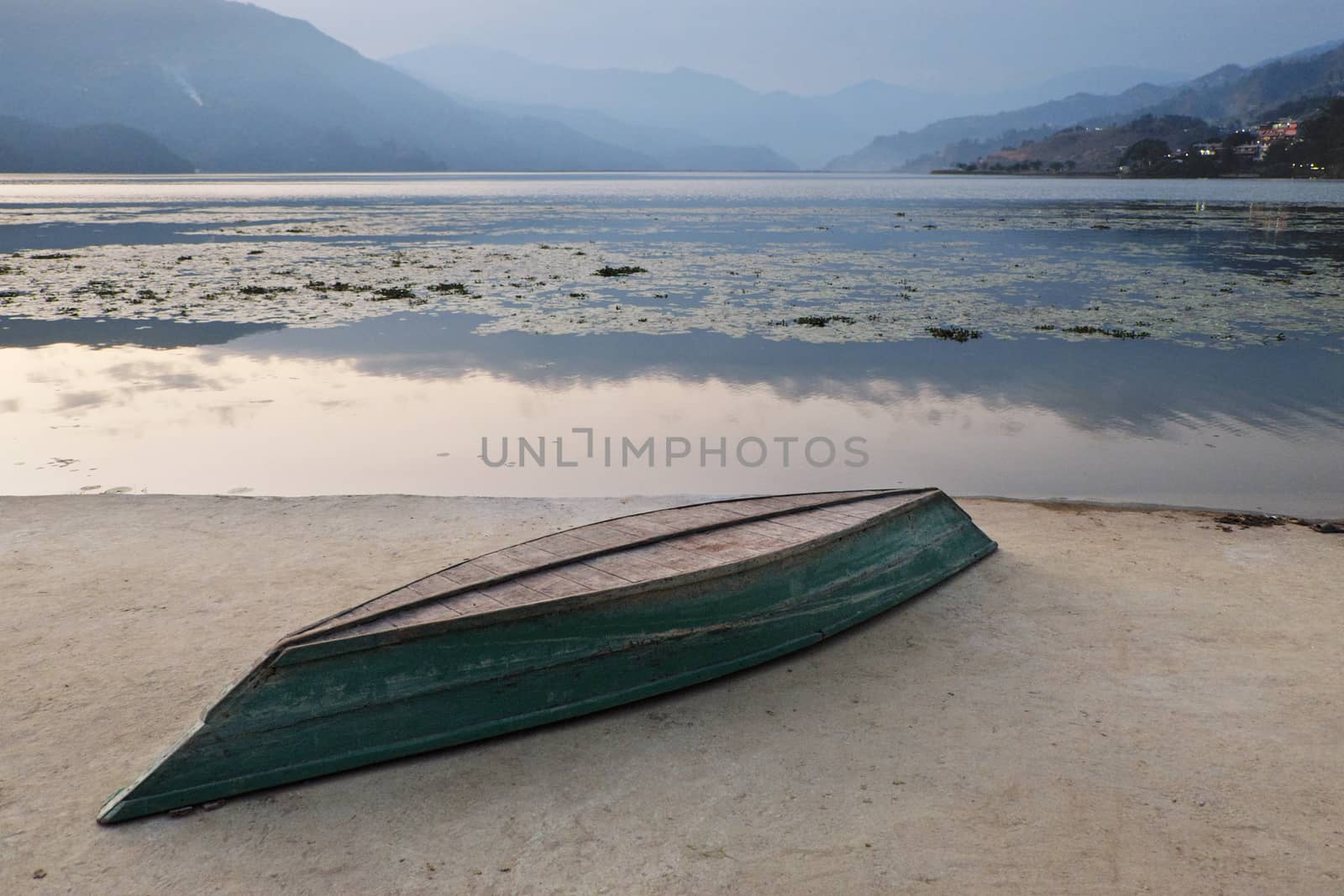 An inverted boat on a concrete embankment on the shore of a mountain lake at sunset.
