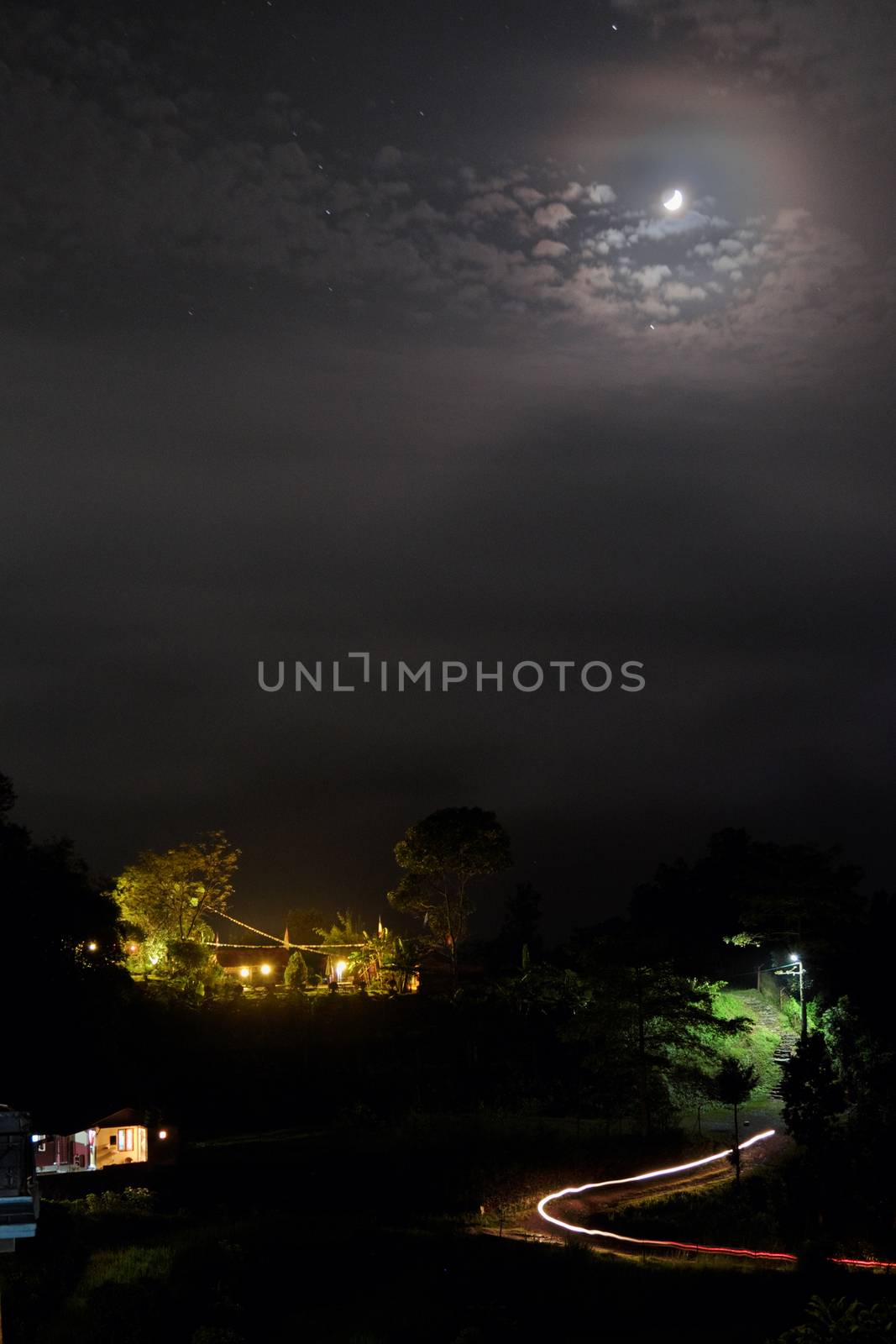 Night landscape with the moon, clouds and lighted buildings.